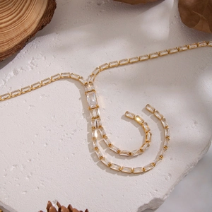 Elegant gold bamboo tassel necklace with zircon inlays on white textured stone