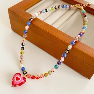 Macro shot of colorful beaded necklace with a red glass heart pendant on wood