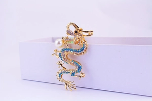 Detailed view of a golden dragon keychain with blue rhinestones and a white pearl accent