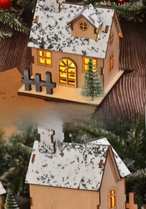 Close-up of lighted wooden Christmas house with snow-dusted roof and warm LED glow