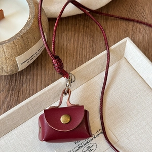 Close-up of a burgundy leather mini bag pendant with a gold snap and braided cord