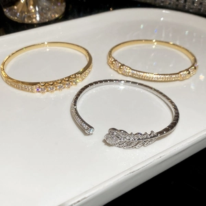 Close-up of gold-plated bracelets and silver feather bangle with cubic zirconia on a ceramic tray