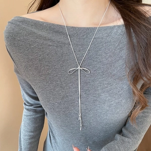 Détail d'un collier nœud argenté avec des glands sur un pull en tricot gris chiné