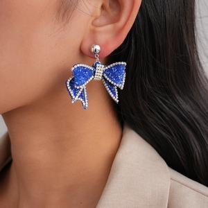 Elegant blue bow stud earring with crystal embellishments worn by model in a macro shot