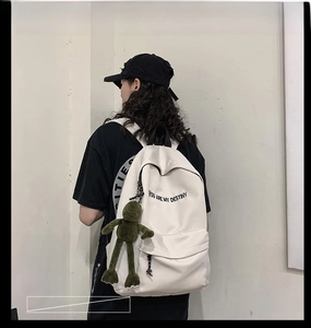 Détail du sac à dos en toile crème avec texte imprimé et pendentif en peluche grenouille