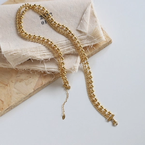 Close-up of golden multi-layer beaded necklace with lobster clasp on wood background