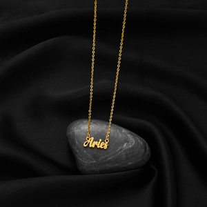Close-up of golden Aries pendant with vintage cursive font on black silk background