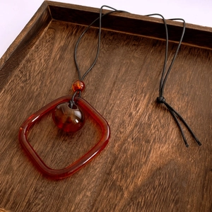 Détail macro d'un pendentif carré en acrylique ambré sur un cordon tressé fin