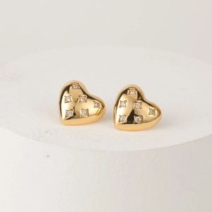 Detailed view of gold heart-shaped stud earrings with sparkling clear crystals on white stand