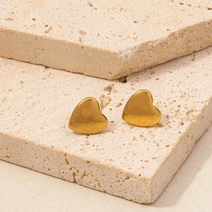 Golden heart-shaped stainless steel earrings on a textured beige stone background