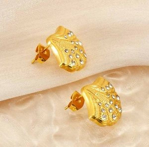Macro view of gold plated shell earrings with diamonds on silk fabric background