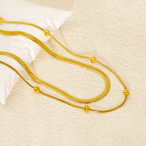 Detail of gold double-layer necklace featuring a flat snake chain and delicate beaded link