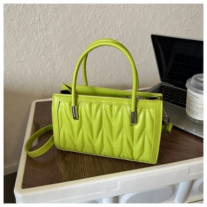 Detail of neon green pleated handbag with V-quilted pattern on a rustic wooden desk