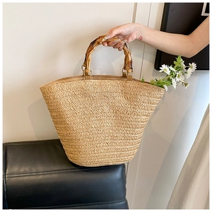 Detail of hand-woven straw tote bag featuring bamboo handles and a white daisy accent