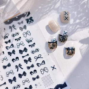 Close-up of black bow and lace nail stickers with polished marble and fabric background