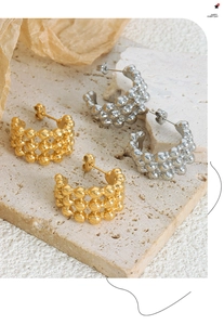 Close-up of gold and silver C-shaped earrings with triple-layered metal bead textures