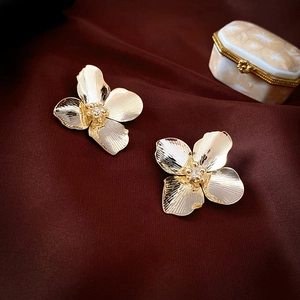 Detailed macro view of gold flower earrings with zircon centers on dark silk fabric