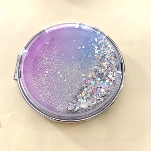 Detail of a round folding compact mirror with purple glitter quicksand and star sequins