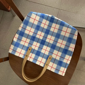 Detail view of blue plaid cotton tote bag with khaki leather straps and metal rivets