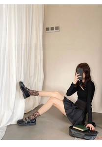 Dettaglio di calze in pizzo marrone abbinate a scarpe Mary Jane nere e gonna a pieghe
