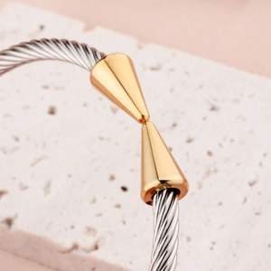 Adjustable titanium steel cable bangle featuring polished gold-tone cone ends