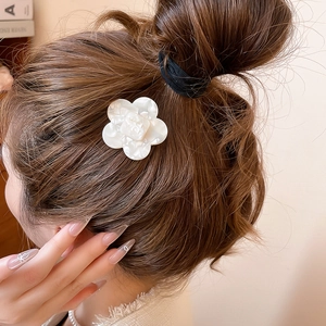 Detailed view of a white resin camellia flower hair clip worn on brown hair for styling