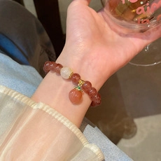 Dettaglio macro di un bracciale di perline con cristalli rossi e ciondolo a pesca