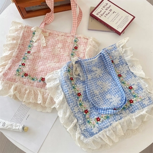 Detail of floral embroidery and lace trim on pink and blue plaid canvas tote bags
