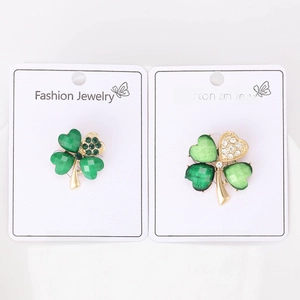 Detailed view of green and gold clover brooches with rhinestones on a card