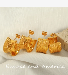 Detailed macro view of 18K gold pleated texture C-shape earrings on white silk fabric