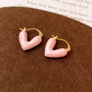 Détail des boucles d'oreilles cœur en émail rose plaquées or sur fond de feutre brun