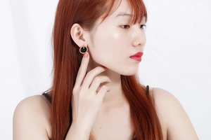 Close-up of a model wearing a round black crystal stud earring with golden metal edge