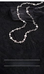 Detail of silver plated poker motif necklace showing heart and clover links on black sand