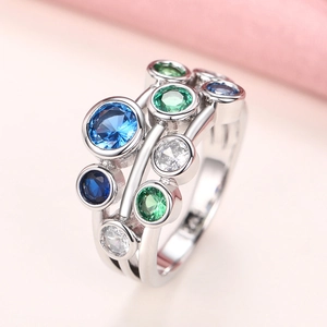 Silver multi-layered ring with green and blue round gemstones on a soft pink background