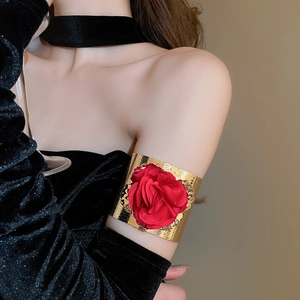 Detail view of a metallic gold arm cuff featuring a vibrant red fabric flower decoration