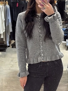 Women's gray knit cardigan sweater with ruffle collar and cuffs on a person in store
