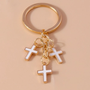 Golden keychain with three white enamel cross pendants on a minimal beige background