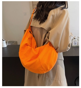 Detailed view of the large orange nylon dumpling bag worn over a beige coat