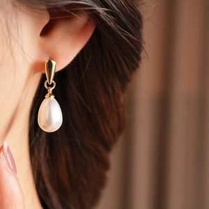 Close-up of elegant gold drop earrings with white water-drop pearls on a model