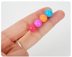 Détail d'une bague dango créative avec perles en résine colorées portée sur fond gris