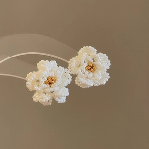 Macro view of handmade camellia pearl beaded flower earrings with gold bead centers