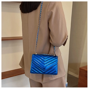 Detail of blue chevron quilted bag with metallic chain strap worn on shoulder
