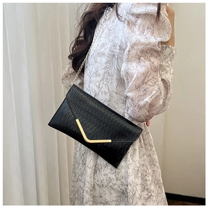 Détail de la texture noire ondulée sur un sac enveloppe avec boucle en V en métal doré