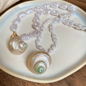 Detail of baroque pearl necklaces with natural spiral seashell pendants on ceramic plate