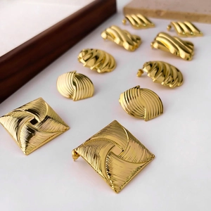 Macro detail of geometric gold metal stud earrings with textured square and oval designs