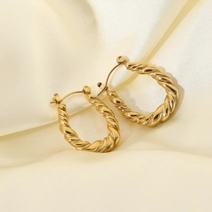 Macro detail of gold-plated stainless steel twisted hoop earrings on white silk