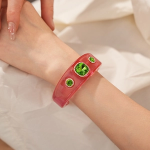 Detail of wide pink resin cuff bracelet featuring emerald green crystals and rhinestones