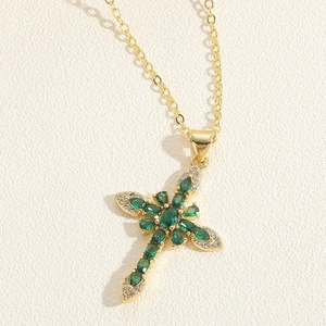 Macro shot of gold cross necklace with vibrant green stones and white crystal halo detail
