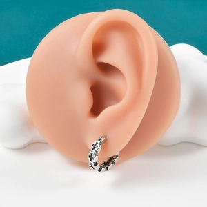 Detail of vintage silver ear cuff with embossed cross pattern on a silicone ear model