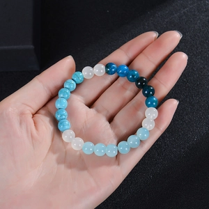 Hand holding 8mm blue apatite and turquoise beaded bracelet on a black surface